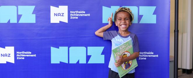 Child wearing crown and smiling, holding abook