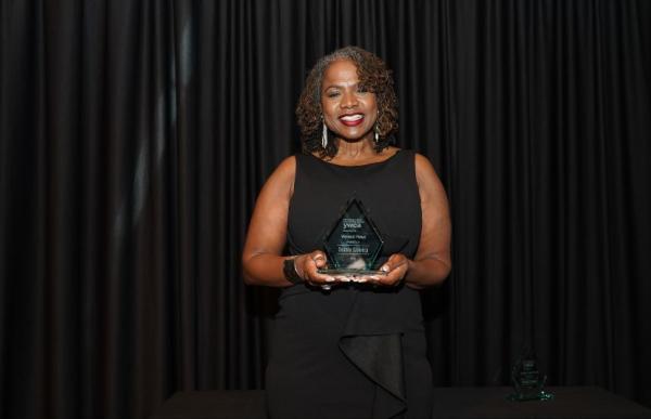 Woman stands against black backdrop holds award