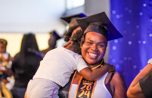 Woman smiling wearing a graduation cap holding a child.
