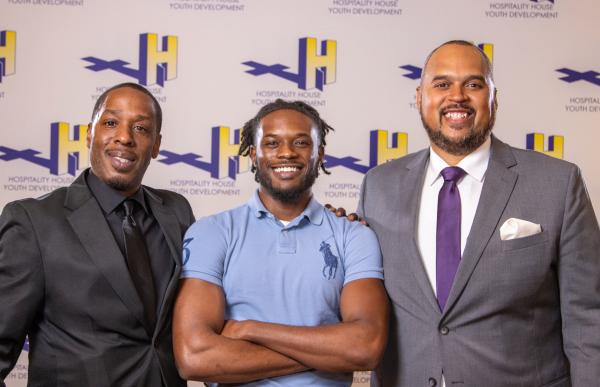 Three men stand together, smiling.