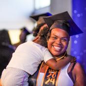 Woman smiling wearing a graduation cap holding a child.