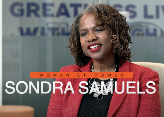 Woman sits, smiling at camera, with overlayed text reading "Woman of Power: Sondra Samuels"