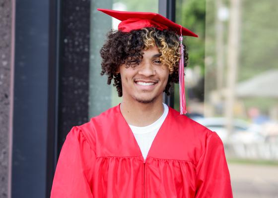 Student stands in red cap and gown