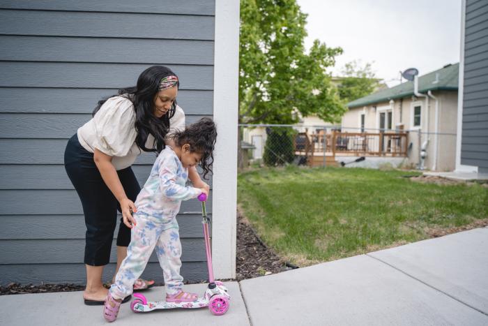 A young mom helps her daughter on her scooter.