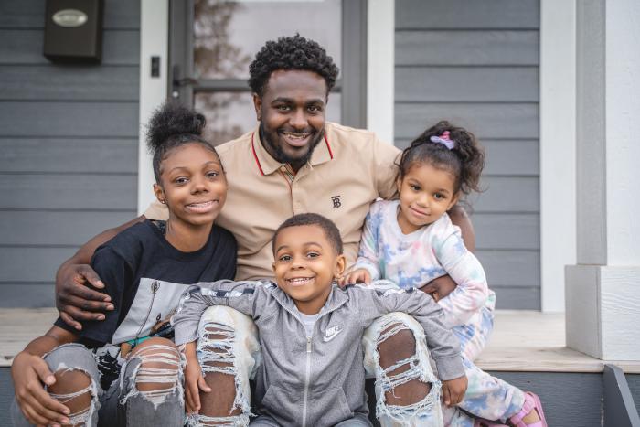 A dad with his three kids sit on the front steps of their home.