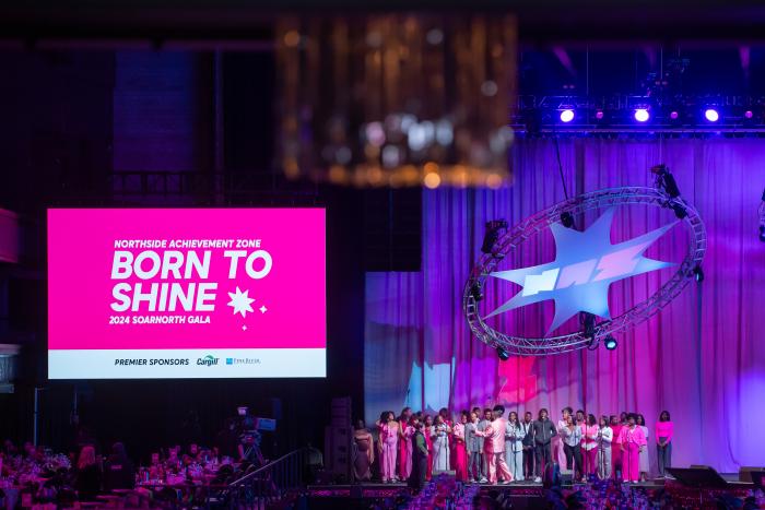 Choir onstage near a screen reading "Born to Shine"
