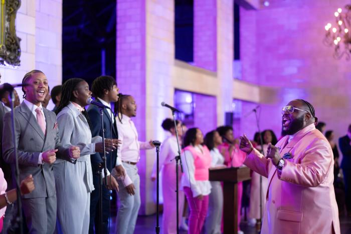 A choir sings, led by a director