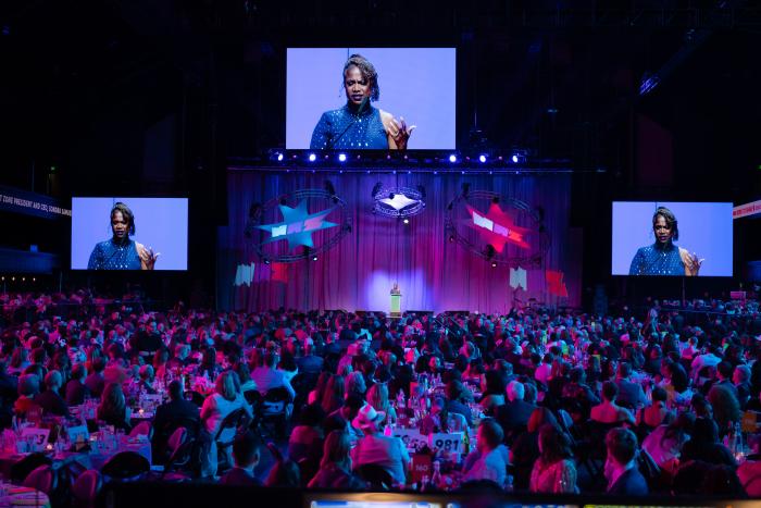 Three screens showing the image of a woman at a podium