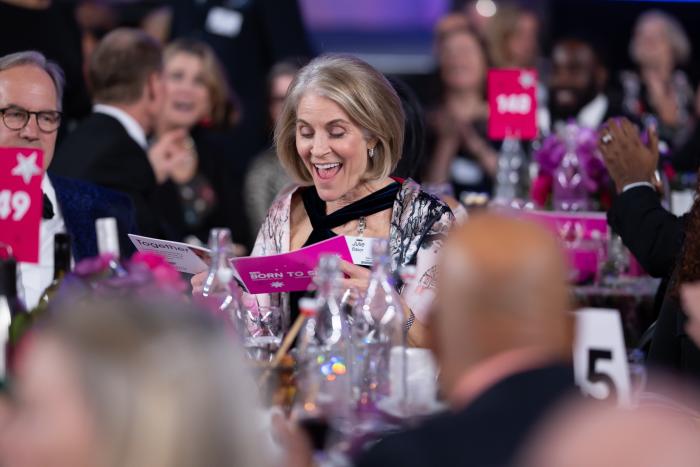 A woman, surrounded by others, smiles at something in front of her