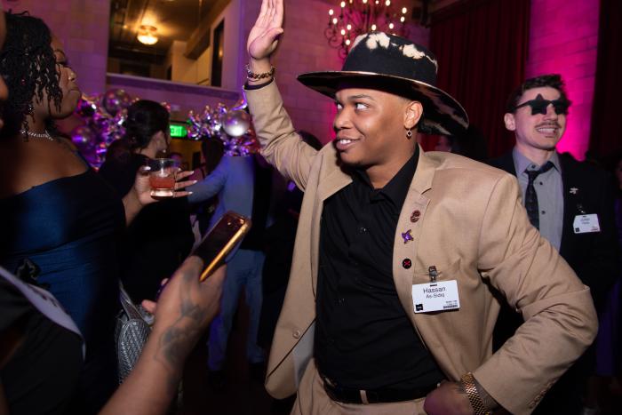 A man wearing a hat dances, hand in air and hand on hip