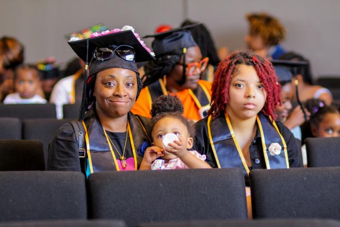 Graduate mother in cap sits next to and with her children.