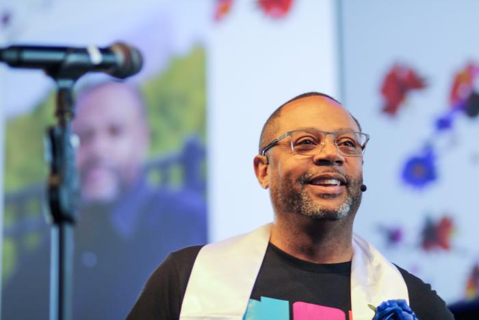 Man wearing graduation stole smiling in front of a microphone.