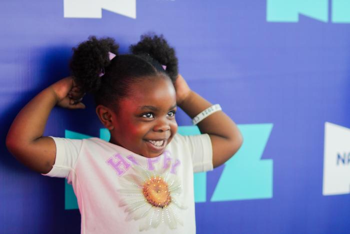 A young girl flexing in front of a blue background.