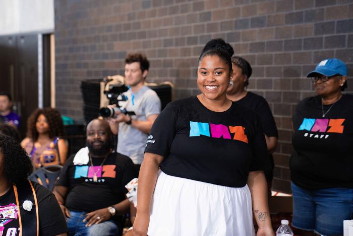 Woman stands and smiles, wearing a "NAZ" t-shirt.