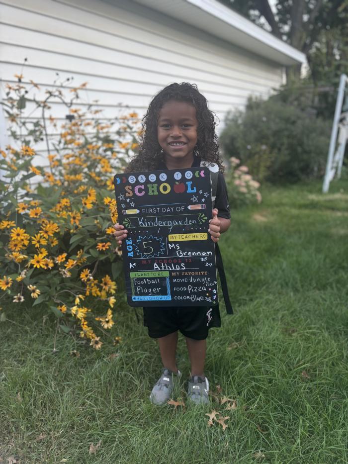 Young student stands holding a school sign