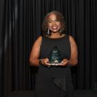 Woman stands against black backdrop holds award